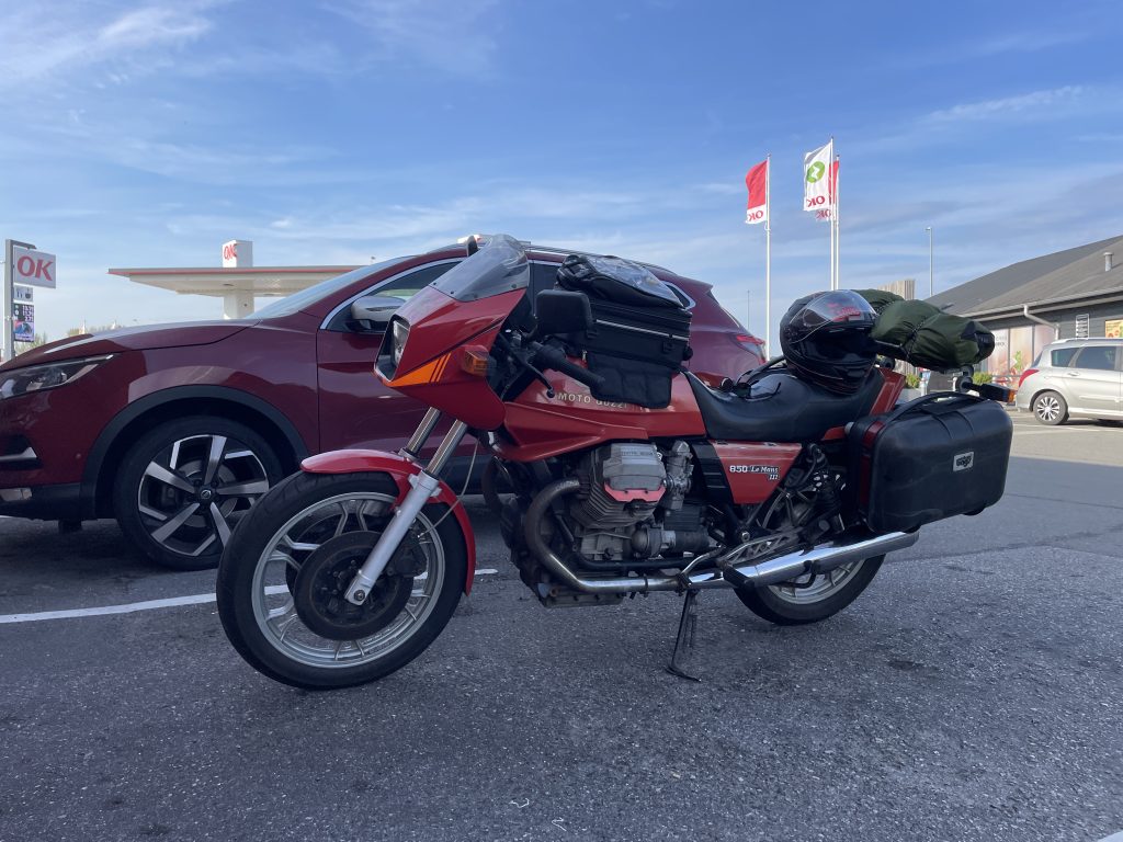 Uffes røde Le Mans III med tanktaske, sidetasker og telt monteret på bagagebæreren. Hjelmen ligger på sædet. Billedet er taget ved OK-tanken i Nyborg.