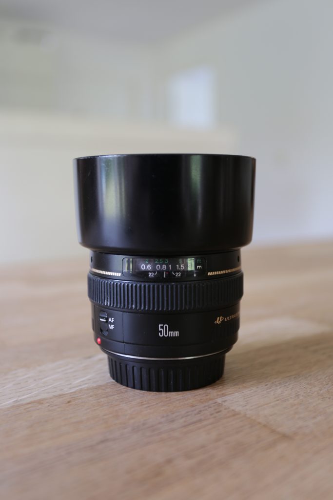 EF50mm f/1.4 USM, stående på bord, med fronen opad. Man kan se  objektivets afstandsskala og fokusring. Objektivet har monteret modlysblænde (lens hood).